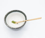 Chashaku de bambú midiendo 1 gramo de matcha sobre un cuenco de cerámica