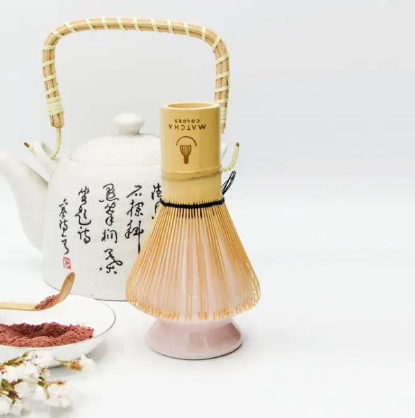 Batidor Chasen de bambú con soporte cerámico rosa. Accesorio esencial para la ceremonia del té, con tetera japonesa de fondo