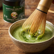 Primer plano del chasen batiendo matcha con espuma fina, lata de Japanese Matcha Premium detrás - campaña IA